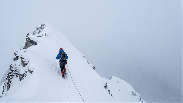 A climber ascends a snowy mountain ridge in harsh winter conditions.