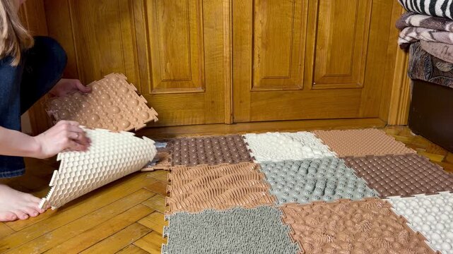 Woman rolling up a modular orthopedic sensory mat on a wooden floor, home cleaning and organization.