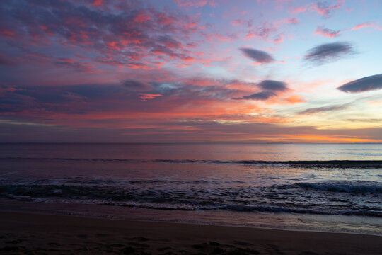 Amanecer sobre el mar con cielo en tonos rosados, morados y azules reflejados en el agua tranquila.