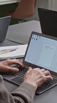 Vertical over shoulder shot of elderly man slowly typing on laptop keyboard and inputting text into document online while attending computer literacy class