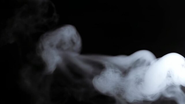 White smoke moves gently upward in a dark area. The smoke forms changing shapes as it swirls and shifts in the air. The focus stays on the smoke's movement