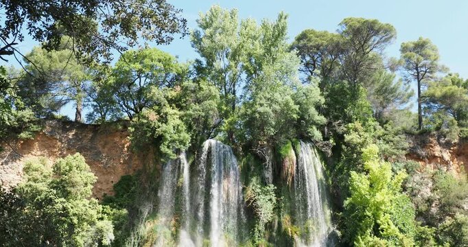 The waters of the Bresque River at Sillans-La-Cascade transform into waterfalls emerging from a wild forest and plunging from an ochre-colored cliff, creating an impressive and magical setting