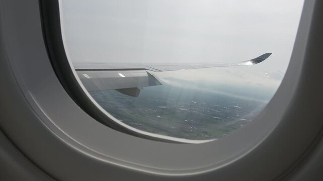 Aircraft window perspective: the plane is deploying inner flaps for landing, forming wake turbulence.