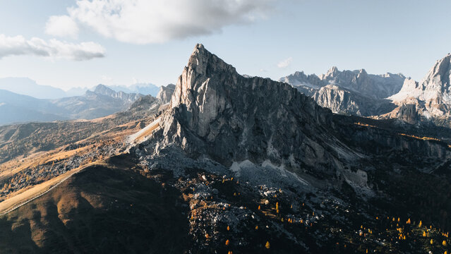 Aerial view of the sharp rocky peak of Passo Giau surrounded by autumn larches and the rugged mountain landscape of the Dolomites in Colle Santa Lucia, Veneto, Italy.