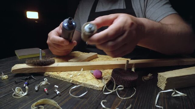 Skilled craftsman uses rotary tool to attach different sanding attachments while working on wood pieces in a dimly lit workshop setting