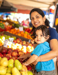 Fototapeta premium The mother helps her child select a piece of fruit at the market, hands touching fresh produce.