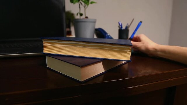 Businesswoman working in office at the table with laptop and stack of books. Woman hand writing in notebook holding pen in hand sitting at the desk. Education, business, study concept. Closeup