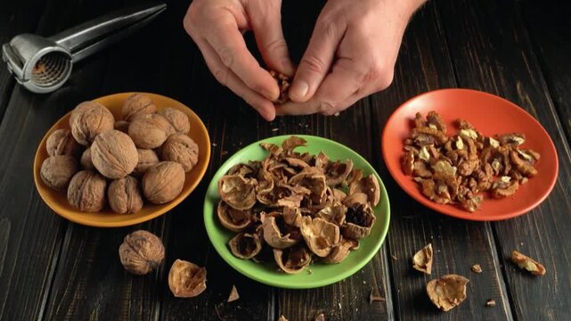 Hands cracking walnuts and separating shells from nuts on a wooden table with colorful bowls and a nutcracker in the background