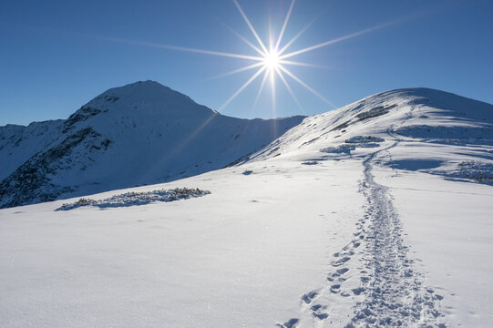 View of Volovec in Western Tatras with snow-covered peaks and a bright sun star over a snowy trail in Witow, Lesser Poland Voivodeship, Poland.