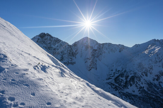 View of Volovec in Western Tatras with snow-covered peaks under a bright sun with a starburst effect and clear blue sky Witow, Lesser Poland, Poland.