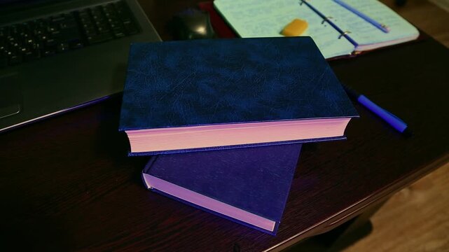 Stack of books, laptop with blue pen on the education, business wood desk indoors. Closeup