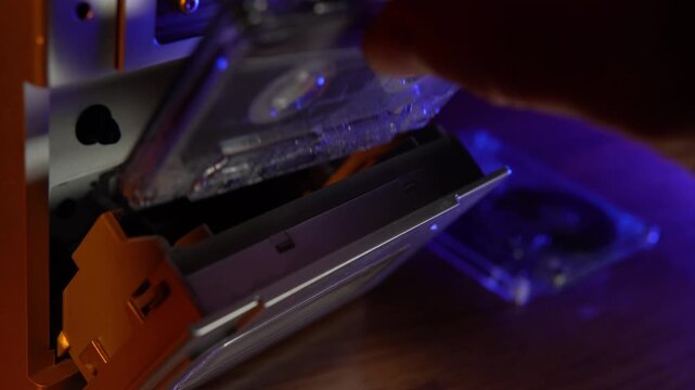 Opening a vintage cassette deck to change an audio tape under neon studio lights.