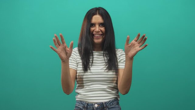 Woman with long dark hair showing open hands toward camera in a studio, palms up and fingers splayed while smiling broadly in a striped tee; joy playfulness.