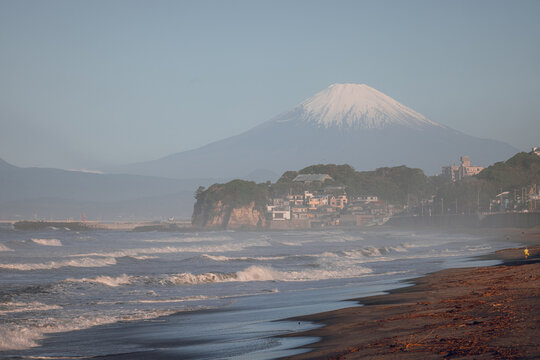 View of Shichirigahama Beach with waves crashing on the shore and the snow-capped peak of Mount Fuji in the distance Kamakura, Kanagawa, Japan.