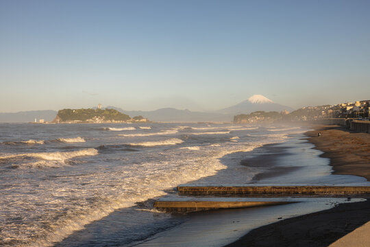 View of Shichirigahama Beach with rolling waves and Enoshima island under a clear sky with Mount Fuji in the distance Kamakura, Kanagawa, Japan.