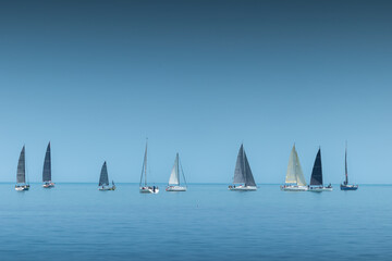 Naklejka premium Sailing yachts and sailboats aligned on a calm blue sea horizon during a regatta