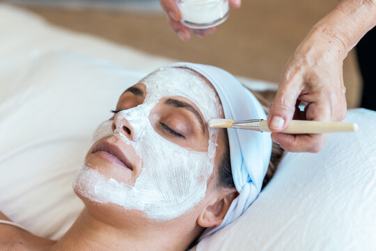Beautiful young woman with clay facial mask in beauty spa. Detox ritual.