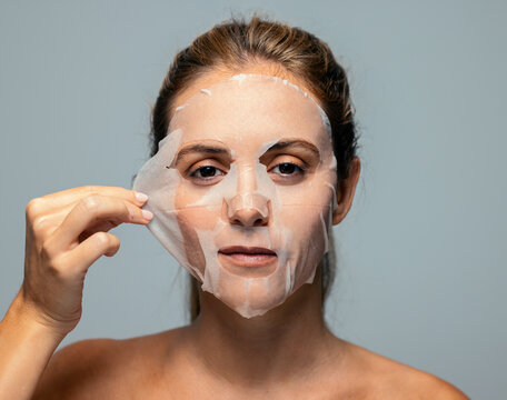 Pretty woman removing the hydrating face maskisolated grey background