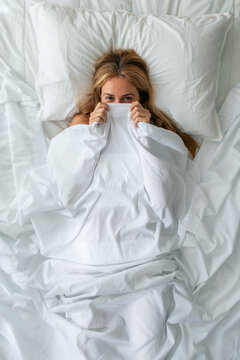 Funny woman playing and covering herself while looking at the camera in bed at home.