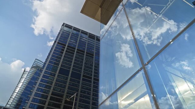 Low angle smooth cinematic dolly movement between modern glass skyscrapers in business district, corporate architecture, urban growth, financial success and contemporary city development