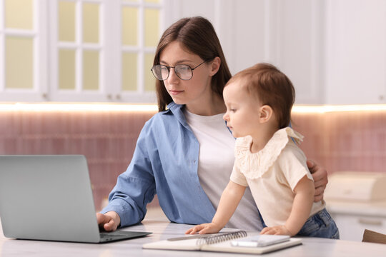 Young mother with her baby working in kitchen at home