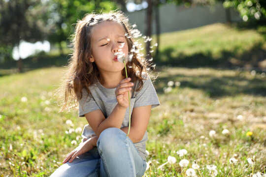 Cute little girl blowing dandelion in park, space for text