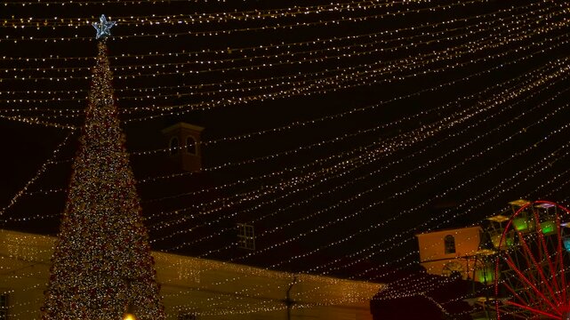 Christmas market lights with tree and ferris wheel at night. Festive christmas market illuminating the night with a large decorated tree, a colorful spinning ferris wheel, and golden string lights