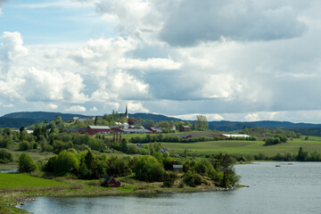 Fototapeta premium Norwegian Farm and Church Overlooking Fjord with Green Fields and Dramatic Sky