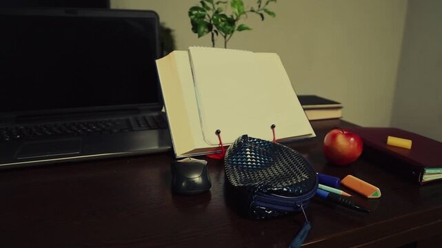 An office desk with a laptop, an open book, and work or study supplies. No people, nobody. A detail of the workspace on a wooden table features a potted plant and an apple. Closeup vintage toned color