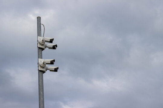 Security camera system mounted on a tall metal pole against a cloudy sky, featuring multiple cameras positioned for surveillance and monitoring purposes