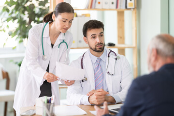 Fototapeta premium Male and female doctors are talking with a mature patient at a clinic. Discussing treatment options