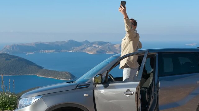 Smartphone signal loss. Young woman stops her car while driving to try to get a smartphone signal, against the backdrop of a panoramic view of the blue sea and distant islands