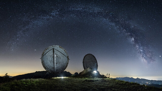View of the large satellite dishes at Monte Giogo under the arch of the Milky Way and a starry night sky in Toscana, Italy.
