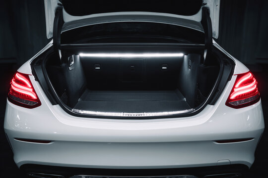 Open trunk of a luxury white modern sedan car with bright white LED illumination strip inside, showcasing a clean spacious empty cargo boot compartment