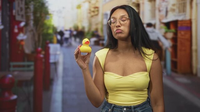 Woman holds yellow rubber duck and pouts lips on street amid storefronts and passersby; boredom whimsy.
