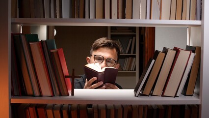 Man in eyeglasses reading a holy book intently between bookshelves with a wooden cross nearby, focused in quiet study and contemplation of faith, theology and spiritual growth © Aliaksandr