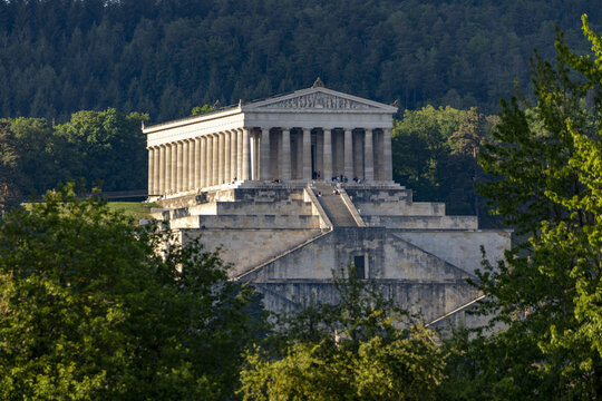 View of the Walhalla memorial with its neoclassical columns and monumental stone steps surrounded by lush green forest in Donaustauf, Bayern, Germany.