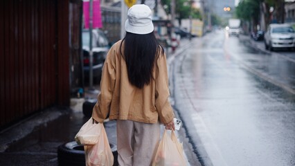 Obraz premium Woman walking on wet street carrying groceries, a rainy day shopping trip