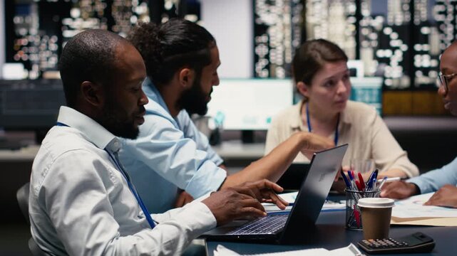 Manager gathering employees in office, evaluating staff performance using tablet, offering task completion feedback. Team leader oversees work done by multiethnic team, reviewing metrics.