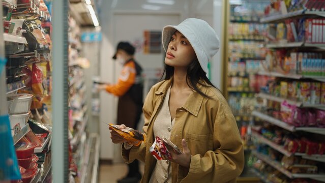 Woman shopping in convenience store choosing food from busy shelves