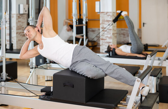 Man with help of informer is engaged in Pilates studio and performs exercises to strengthen muscles of press. Round-robin training for athletes during preparation for competitions