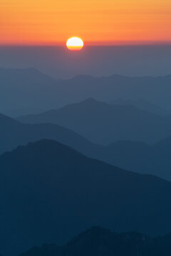 View of the sun rising over the layered mountain peaks and misty valleys of the Yellow Mountains in Huangshan City, Anhui, China.