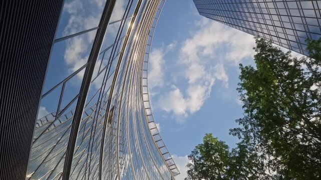 Low angle motion shot of modern corporate skyscrapers with reflective facades and urban greenery symbolizing innovation investment and future city development