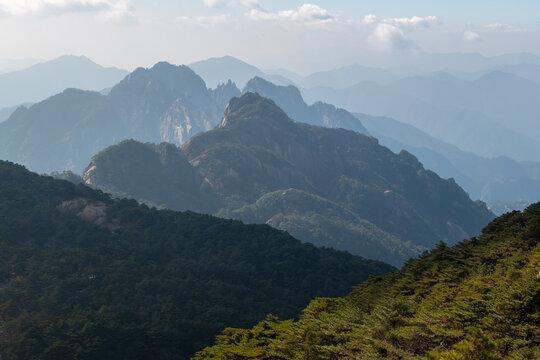 View of the majestic granite peaks and pine-covered slopes of the Yellow Mountain range under a soft hazy sky Huangshan City, Anhui, China.