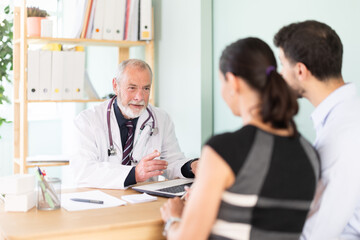 Obraz premium At clinic, couple is at doctors appointment. Senior male medical specialist and patients sit at table and communicate, interview, anamnesis, patient complaints