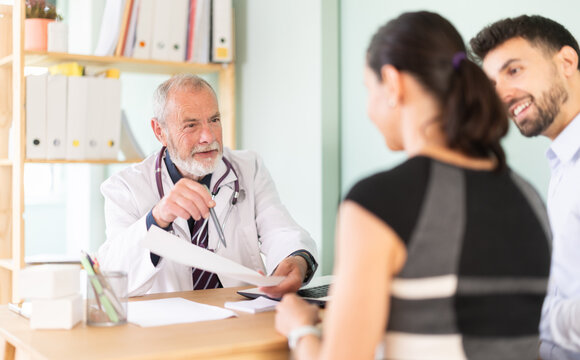 Senior male doctor family patients examine papers, discuss medical tests result. Specialist interprets tests, tells you action plan to achieve goals of treatment. Husband and wife at pre-pregnancy