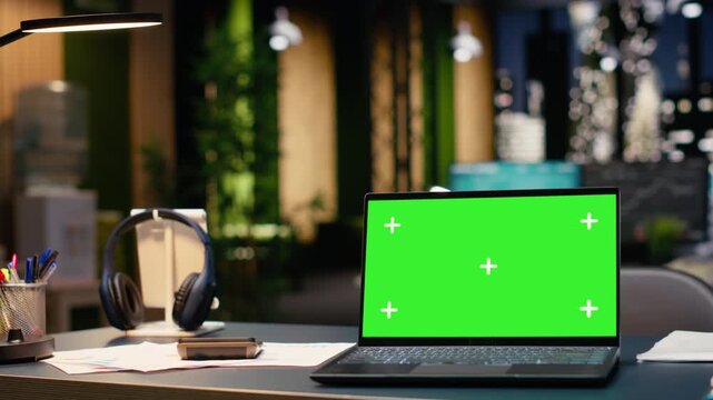 Chroma key on laptop in empty office interior with open space layout and professional design. Large windows reveal vibrant city skyline at night, corporate success and enterprise headquarters.