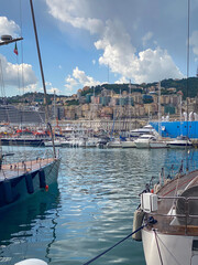 Obraz premium Yachts and sailboats moored in Porto Antico marina with a cruise ship and Genoa skyline against blue sky with clouds, Italy