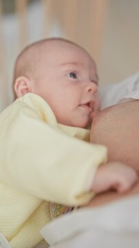 Newborn baby in a yellow onesie latched to mother's breast while breastfeeding inside a building; maternal tenderness.