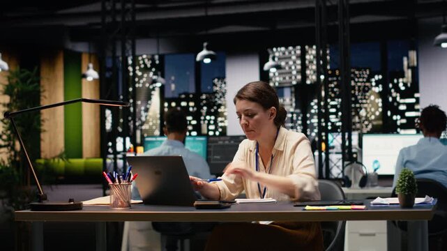 Businesswoman working on project in modern startup office using laptop, happy employee at computer desk analyzing data statistics during business audit late at night. Corporate productivity.